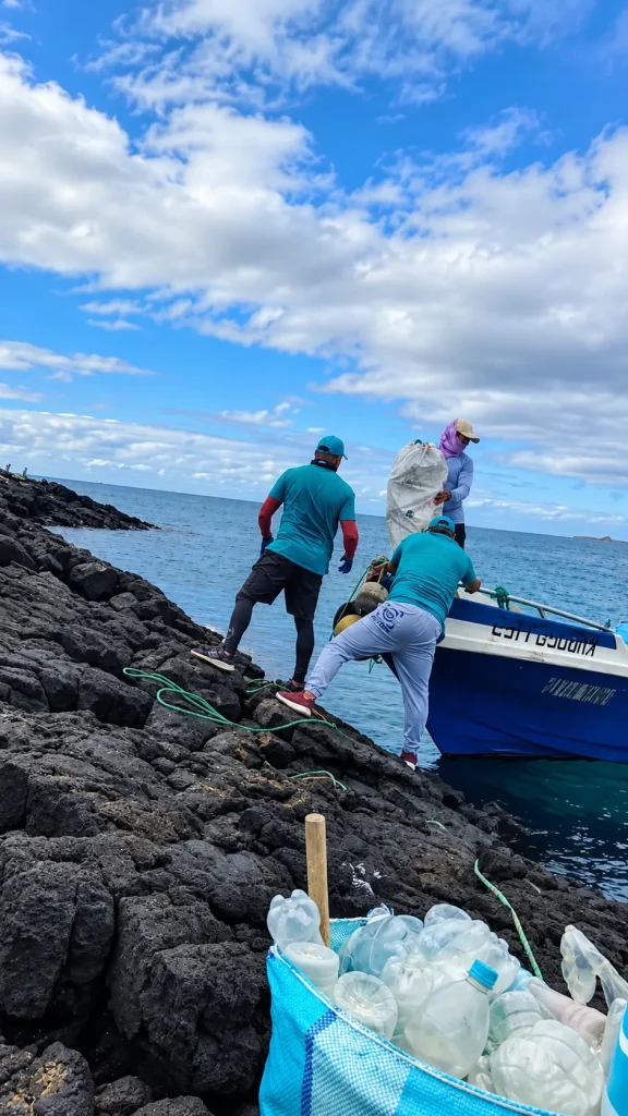 Volunteers loading bags of waste onto a boat from the lava rocks