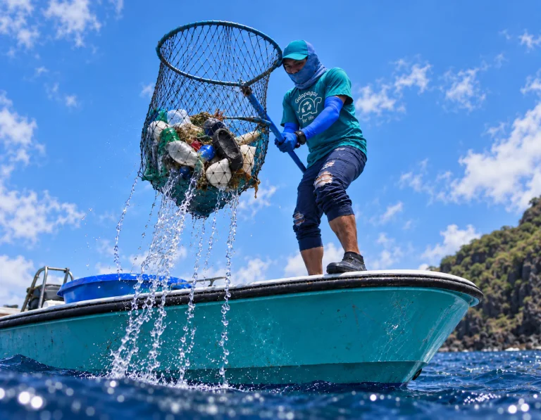 Volunteer on a turquoise boat lifting a net full of plastic waste out of the ocean